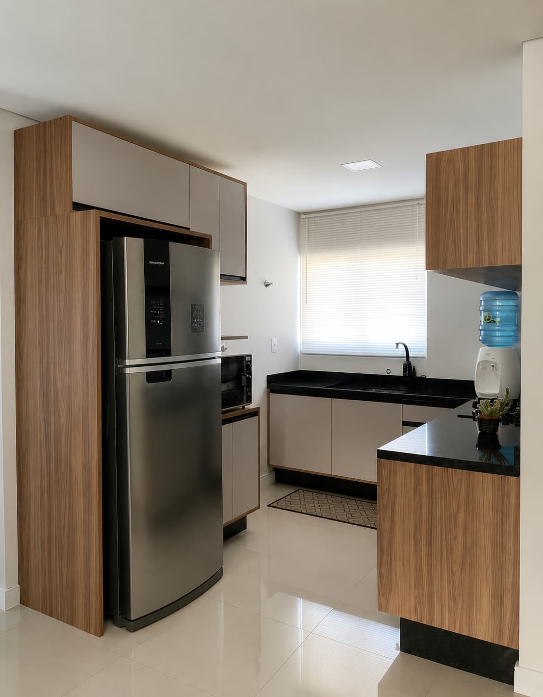 Cozinha compacta com geladeira inox, torre em madeira e bancada preta