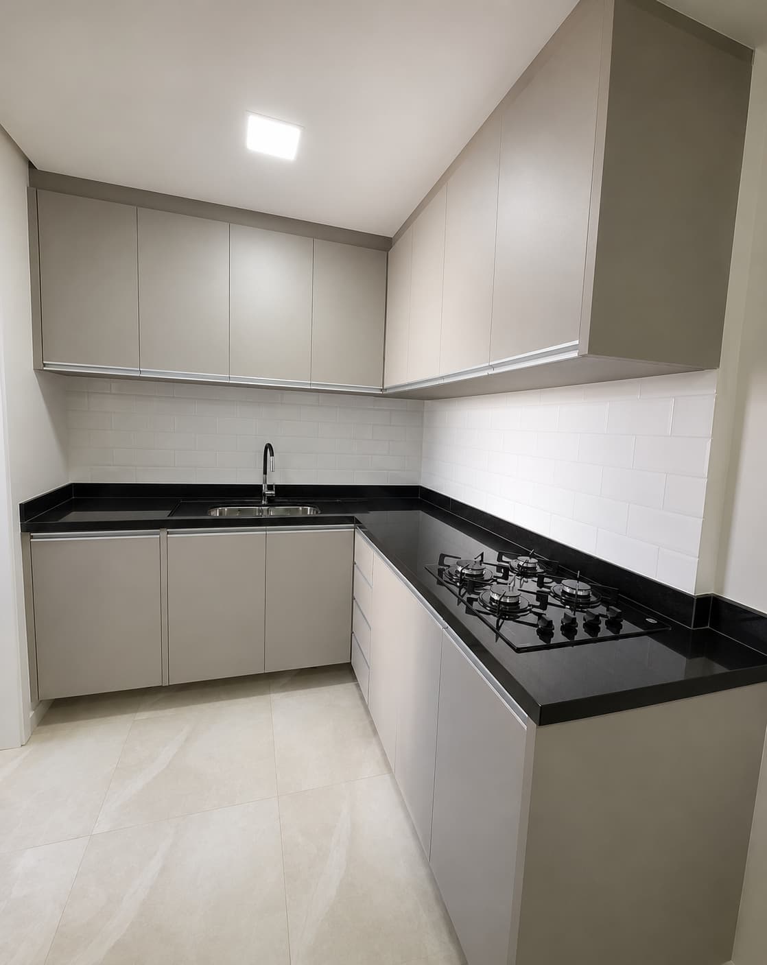 Cozinha planejada cinza com armários superiores, bancada preta e cooktop